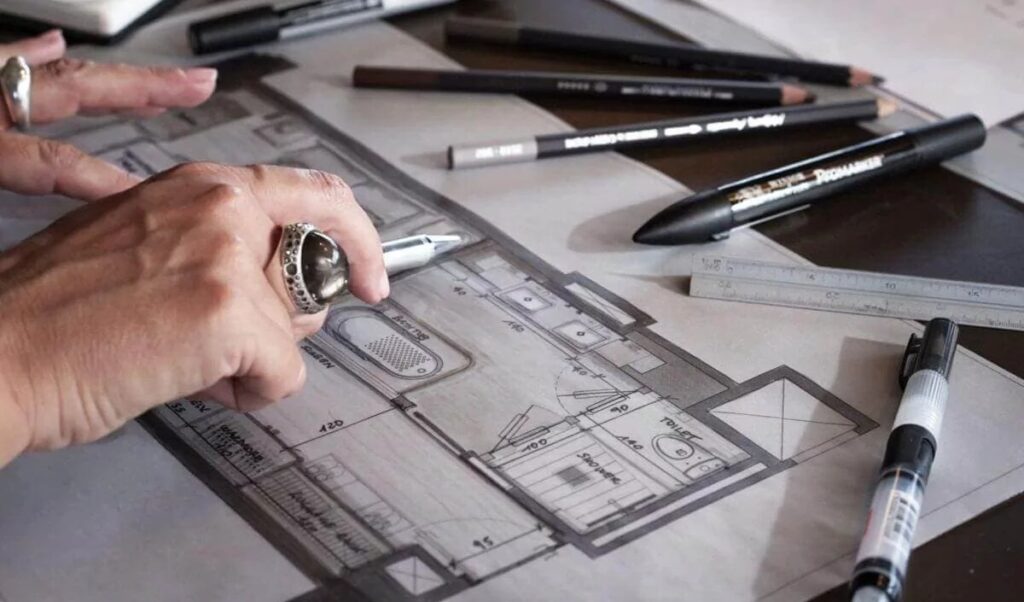 Close-up of an architect reviewing a residential floor plan with drafting tools and pencils on a worktable