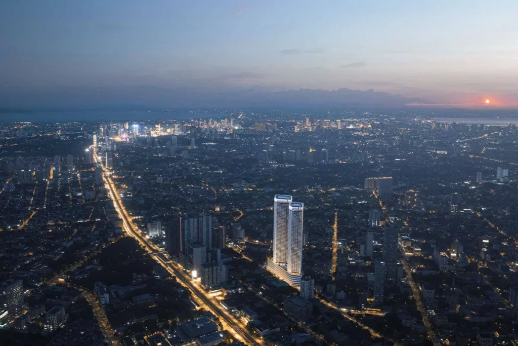 Aerial view of Quezon City at dusk with illuminated roads, urban development, and a prominent luxury residential tower