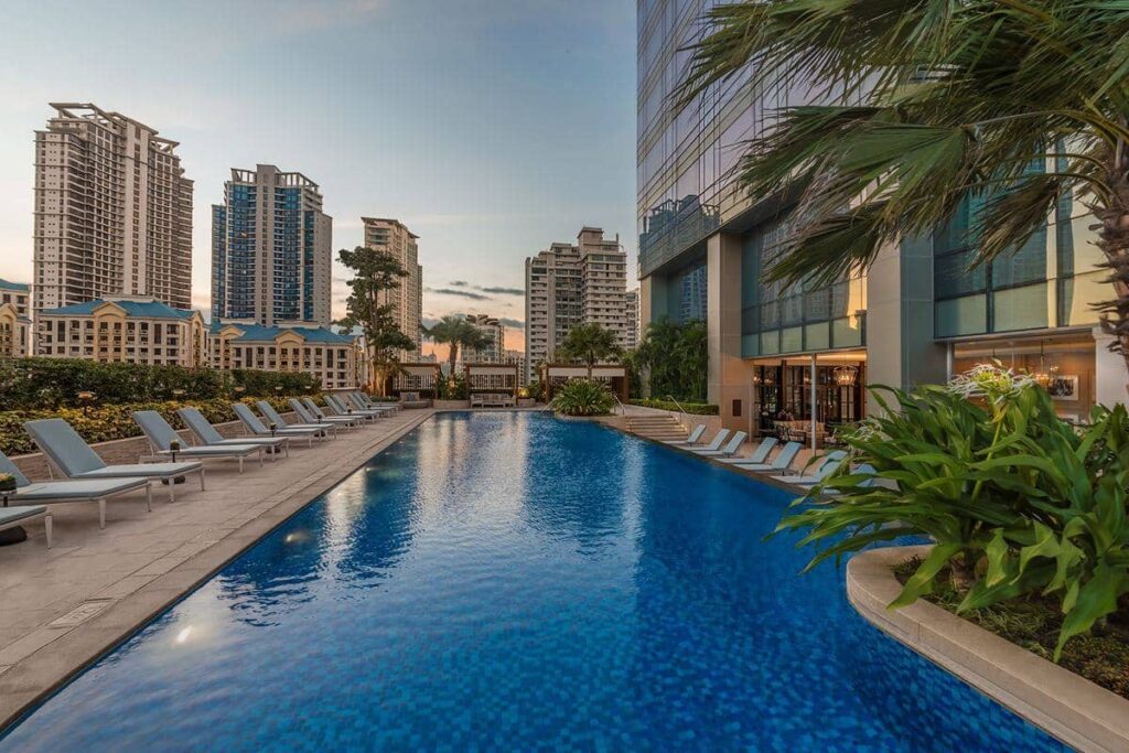 Luxury condominium swimming pool surrounded by high-rise residences, landscaped greenery, and lounge areas
